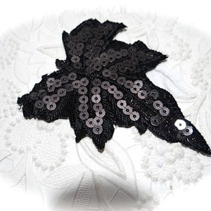 May include: Black sequined leaf applique. The leaf is made of black fabric and is covered in black sequins. It is a great embellishment for clothing, bags, or other crafts.
