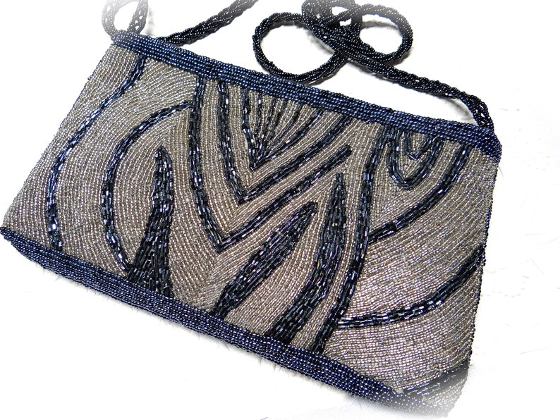 May include: A silver and black beaded evening bag with a geometric pattern. The bag has a long beaded strap.