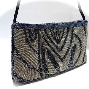 May include: A silver and black beaded evening bag with a geometric pattern. The bag has a long strap and a flap closure.