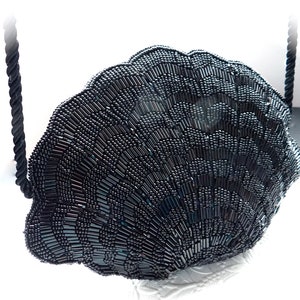 Puede incluir: Un bolso de noche negro de cuentas con forma de concha con una correa de cuerda negra.