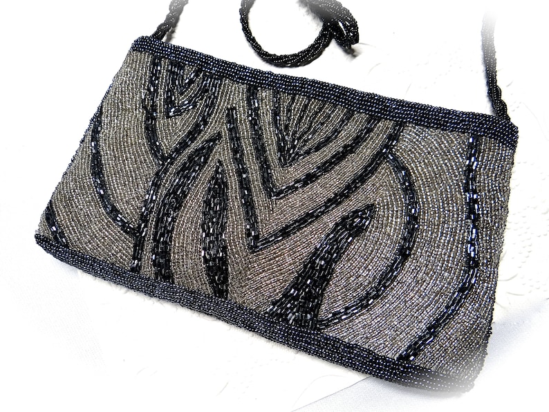 May include: A black and silver beaded evening bag with a geometric pattern. The bag has a black beaded strap.