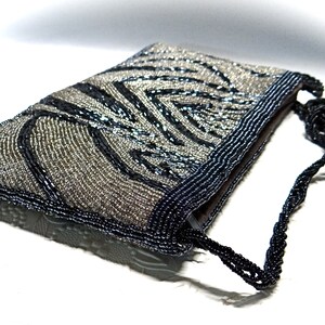 May include: A silver and black beaded evening bag with a black beaded strap. The bag has a zebra-like pattern.