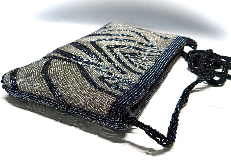 May include: A silver and black beaded evening bag with a black beaded strap. The bag has a zebra-like pattern.