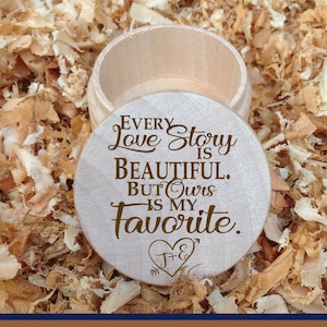 May include: A wooden box with a round lid engraved with the text "Every Love Story is Beautiful. But Ours is My Favorite." and a heart with the initials "J+E". The box is sitting on a bed of wood shavings.