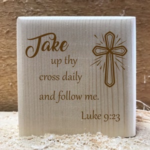 May include: Wooden block with a brown cross and the text "Take up thy cross daily and follow me. Luke 9:23"