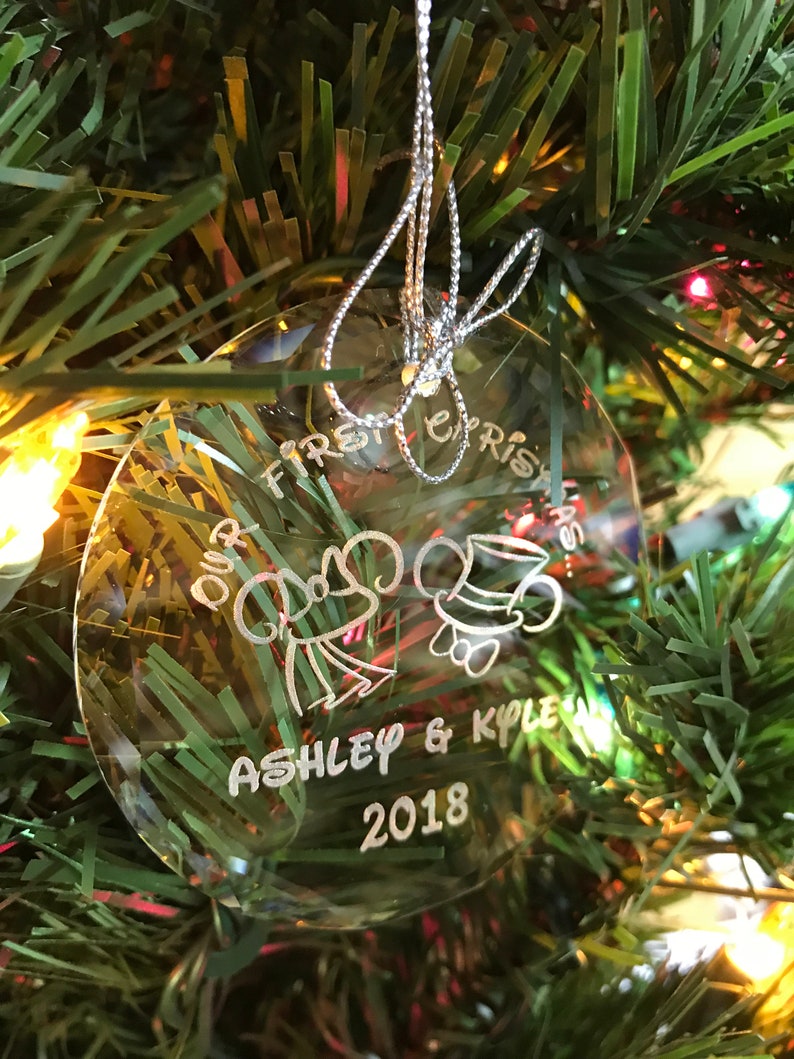 Pu&ograve; includere: Ornamento natalizio rotondo e trasparente con la scritta "Our First Christmas", i nomi "Ashley & Kyle" e l'anno "2018". L'ornamento, sospeso da un filo d'argento, presenta disegni di campana e cappello.