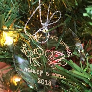 Pu&ograve; includere: Ornamento natalizio ovale trasparente con testo argentato e cordino argentato per appenderlo. L'ornamento dice "Our First Christmas" con i nomi "Ashley & Kyle" e l'anno "2018". Sono incise anche due figure di cartoni animati.