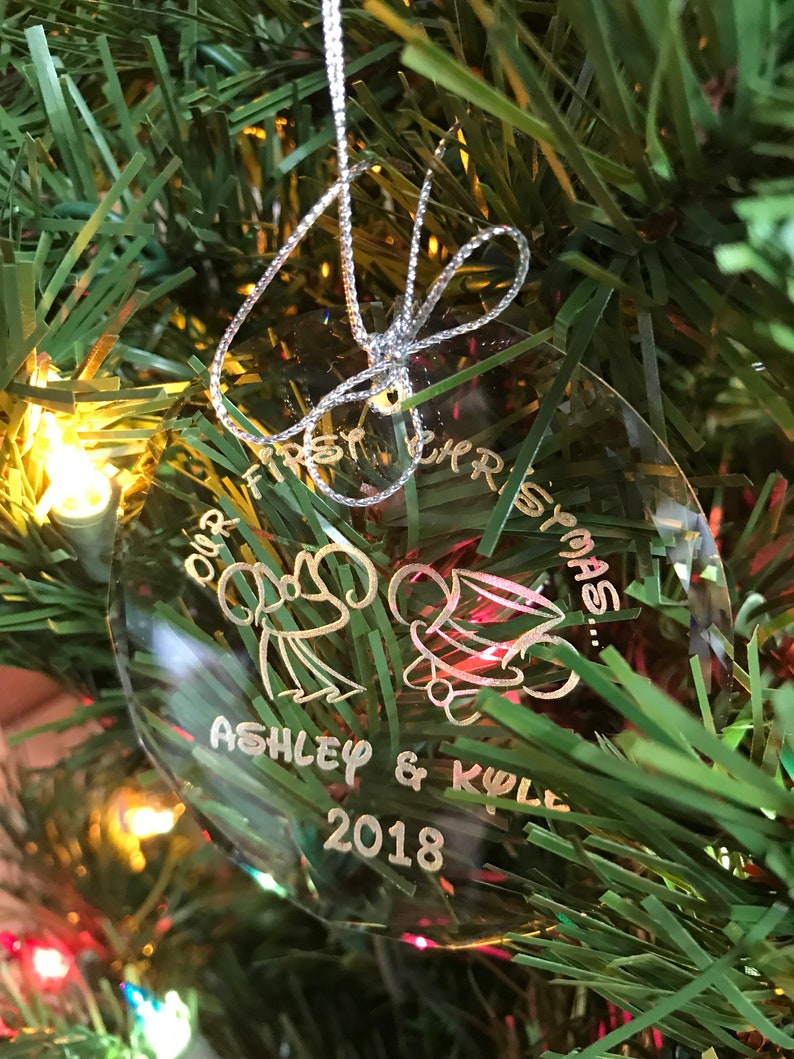 Pu&ograve; includere: Ornamento natalizio ovale trasparente con testo argentato e cordino argentato per appenderlo. L'ornamento dice "Our First Christmas" con i nomi "Ashley & Kyle" e l'anno "2018". Sono incise anche due figure di cartoni animati.