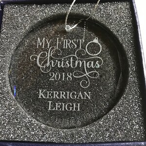 May include: A clear glass Christmas ornament with the text "My First Christmas 2018" and the name "Kerrigan Leigh" engraved on it. The ornament is in a blue box with white foam padding.