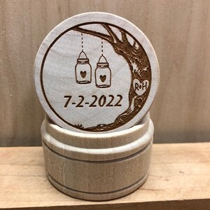 May include: A wooden box with a lid featuring a carved design of a tree with two mason jars hanging from the branches. The jars have hearts inside and the date 7-2-2022 is carved below. The lid also has the initials R+H carved into the tree trunk.