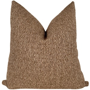 May include: A brown and beige throw pillow with a textured woven fabric.