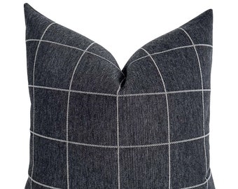 May include: A square, dark grey cushion featuring a grid pattern of thin, white lines. The cushion has a textured appearance and a classic design, suitable for a sofa or bed.