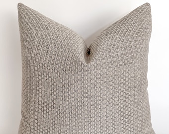 May include: A square throw pillow with a textured, woven fabric in a light gray color. The pillow has a subtle pattern of small squares.
