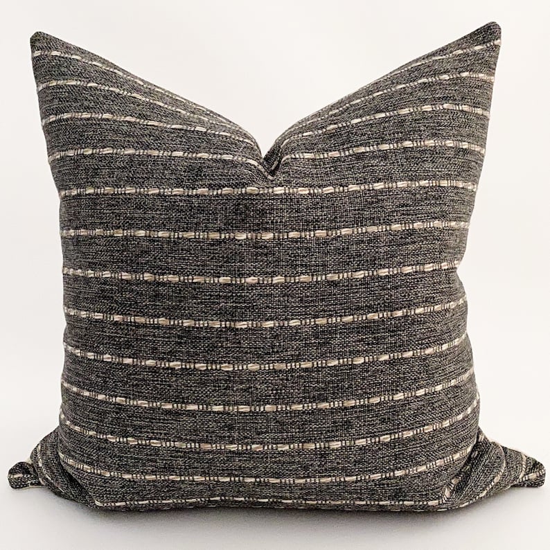 May include: A black and white striped throw pillow with a subtle woven texture. The pillow is made of a soft, comfortable fabric and has a simple, modern design.