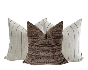 May include: Three decorative throw pillows, two are white with black stripes and one is brown with a textured pattern.