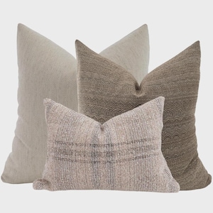 May include: Four decorative cushions in neutral tones. The cushions feature textured fabrics in shades of beige and brown. The cushions have various patterns, including herringbone and woven textures, adding visual interest to the home decor.