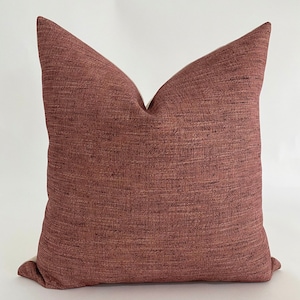 May include: A red and brown textured throw pillow with a white border.