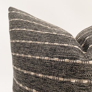 May include: A close-up of a gray and white striped throw pillow with a textured fabric.