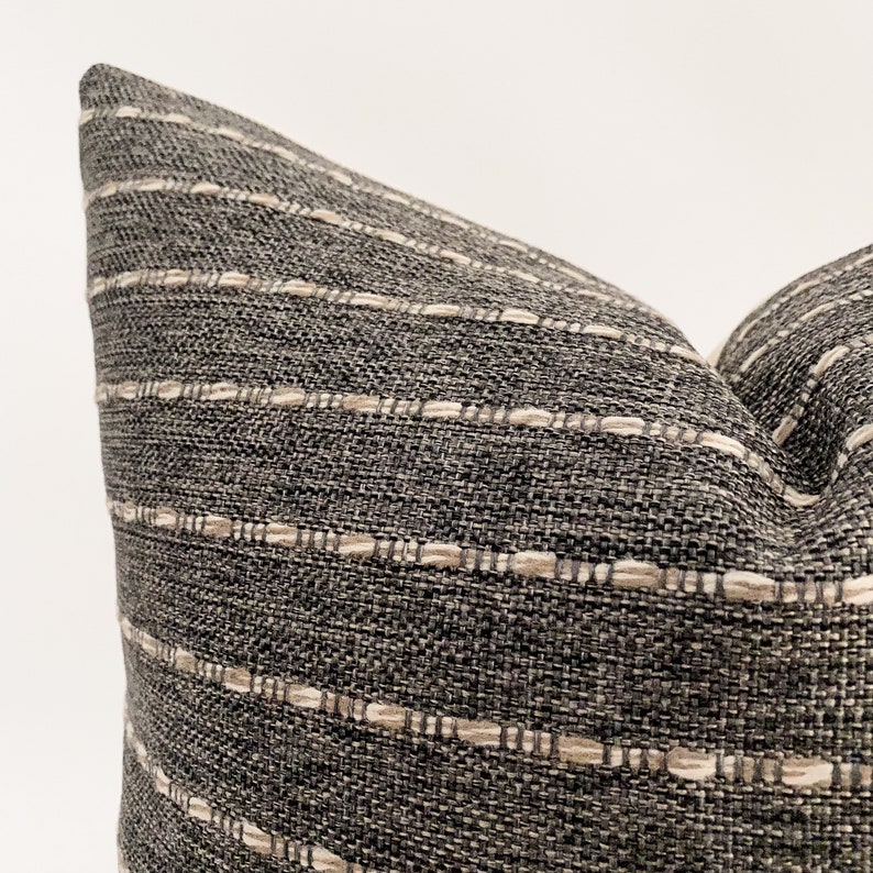 May include: A close-up of a gray and white striped throw pillow with a textured fabric.