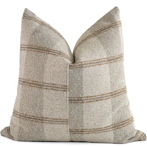 May include: A beige and brown plaid throw pillow with a subtle texture. The pillow is made of a soft, woven fabric and has a square shape.