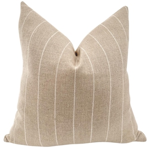 May include: A square cushion in a neutral beige with vertical white stripes. The cushion has a textured appearance, creating a soft and inviting look. Ideal for adding a touch of style to any living space.