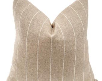 May include: A square decorative pillow in a neutral beige color with vertical white stripes. The pillow has a textured appearance and a soft, inviting look, suitable for adding a touch of style to any living space.