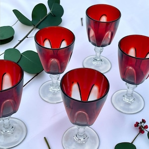 May include: A set of five matching stemmed glasses featuring deep red bowls with clear glass bases and stems. Each glass has a distinct vertical panel design around the lower portion of the bowl, creating a faceted appearance in the red glass.