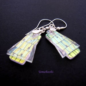 May include: Iridescent earrings with a rectangular design. The earrings feature a layered, geometric pattern in yellow and green, suspended from silver-coloured hooks. The word "Umeboshi" is visible in the bottom right corner.