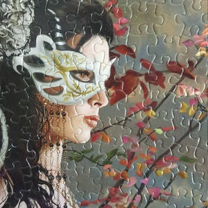 K&ouml;nnte beinhalten: Eine Frau mit langen dunklen Haaren tr&auml;gt eine wei&szlig;e Maskenballmaske mit goldenen Akzenten. Sie tr&auml;gt ein schwarzes und wei&szlig;es Spitzenoberteil und eine Halskette mit Perlen und Ketten. Der Hintergrund ist ein verschwommenes Bild eines Baumes mit rosa und roten Bl&uuml;ten.