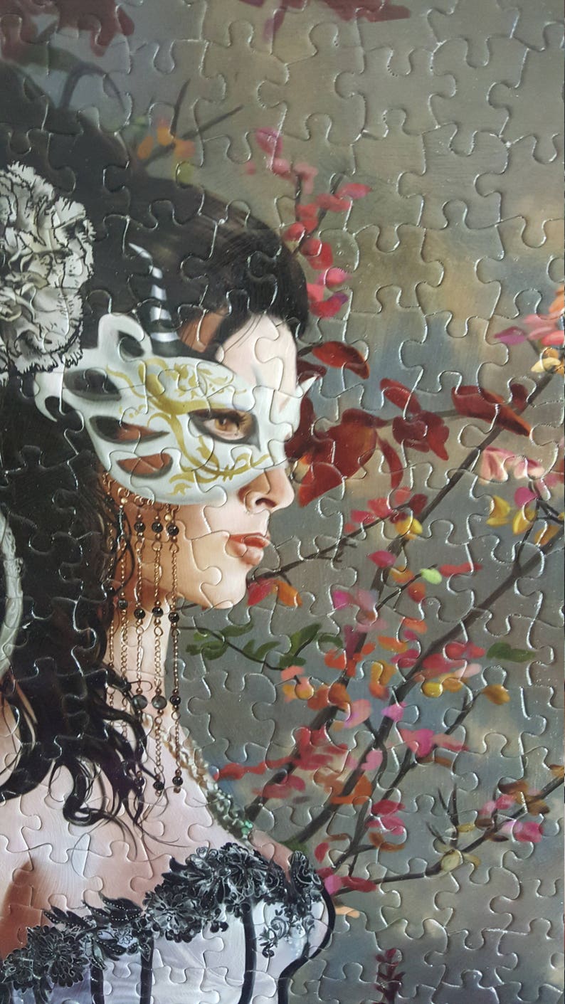 K&ouml;nnte beinhalten: Eine Frau mit langen dunklen Haaren tr&auml;gt eine wei&szlig;e Maskenballmaske mit goldenen Akzenten. Sie tr&auml;gt ein schwarzes und wei&szlig;es Spitzenoberteil und eine Halskette mit Perlen und Ketten. Der Hintergrund ist ein verschwommenes Bild eines Baumes mit rosa und roten Bl&uuml;ten.