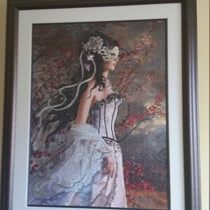 K&ouml;nnte beinhalten: Ein gerahmter Druck einer Frau, die eine wei&szlig;e Maske und ein wei&szlig;es Kleid mit Spitzenbesatz tr&auml;gt. Sie steht in einem Wald mit roten Bl&auml;ttern und einem bew&ouml;lkten Himmel im Hintergrund.