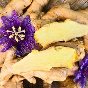 May include: Close-up of fresh ginger root with two slices and two purple passion flowers with yellow centers. The ginger is a light brown color, and the flowers have delicate, fringed petals.
