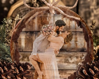 May include: A round wooden ornament featuring a printed photograph of a couple embracing. The man wears a light suit and the woman wears a light dress while holding a floral bouquet. The ornament has a natural wood edge and a jute twine bow on top.