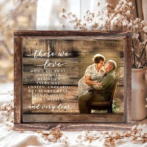May include: A rectangular wooden frame containing a print with a rustic wood-plank background. The text reads: Those we love don't go away, they walk beside us every day. Unseen, unheard, but always near, still loved, still missed, and very dear.