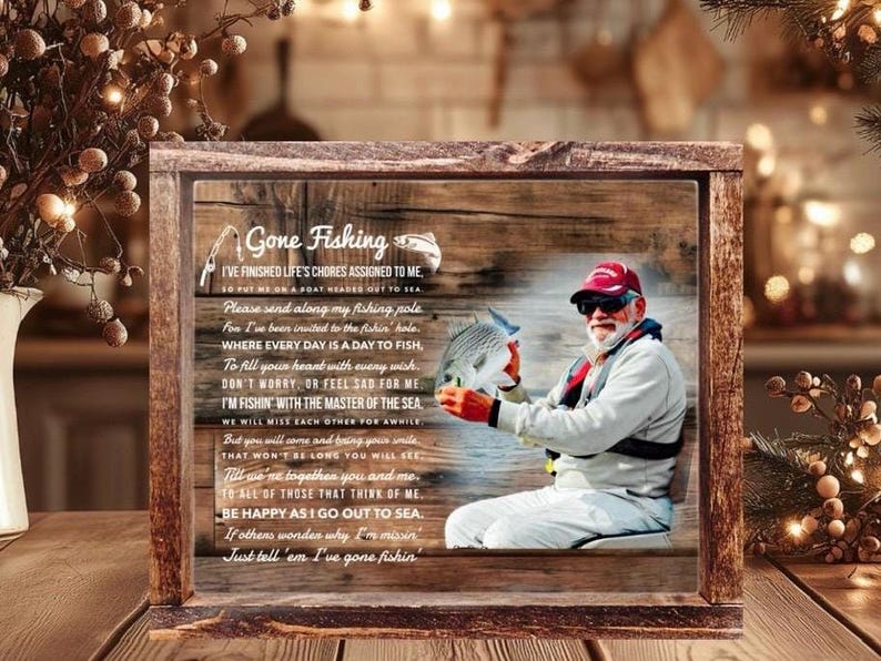 K&ouml;nnte beinhalten: Ein rechteckiges Holzschild mit dem aufgedruckten Bild einer Person mit roter Kappe, die einen Fisch h&auml;lt. Der Text lautet Gone Fishing und enth&auml;lt ein Gedicht &uuml;ber das Angeln. Der Hintergrund zeigt eine rustikale Holzmaserung mit Angelhaken.