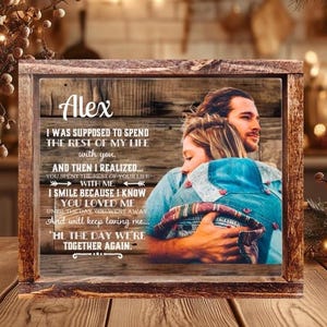 May include: A rectangular wooden frame containing a printed image of a couple embracing. The print features a rustic wood grain background with the name Alex and a memorial poem about love and loss. The frame has a dark, weathered finish.