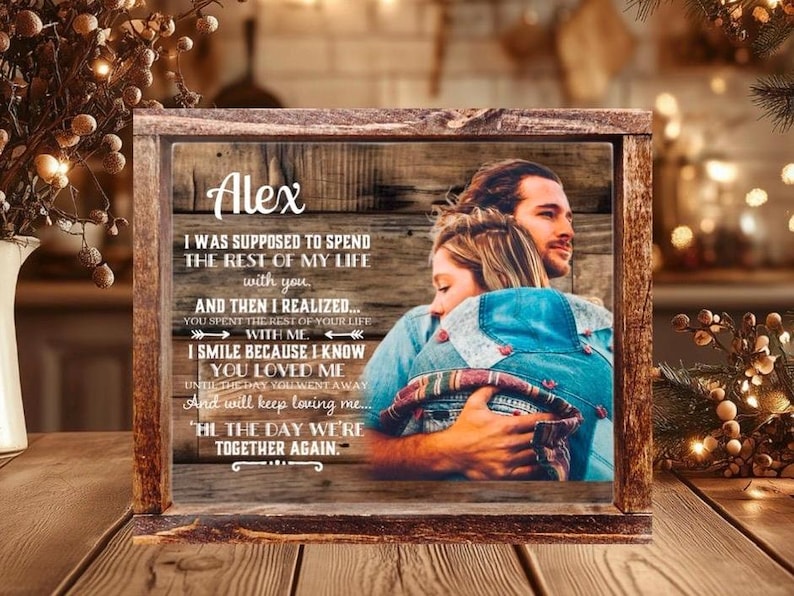May include: A rectangular wooden frame containing a printed image of a couple embracing. The print features a rustic wood grain background with the name Alex and a memorial poem about love and loss. The frame has a dark, weathered finish.