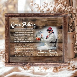 K&ouml;nnte beinhalten: Ein rechteckiges Holzschild mit rustikalem Holzmaserungshintergrund, einem Foto einer Person, die einen Fisch h&auml;lt, und dem Text Gone Fishing. Es enth&auml;lt ein Gedicht, den Namen James Davis und die Daten 3. M&auml;rz 1978 - 3. Mai 2023.