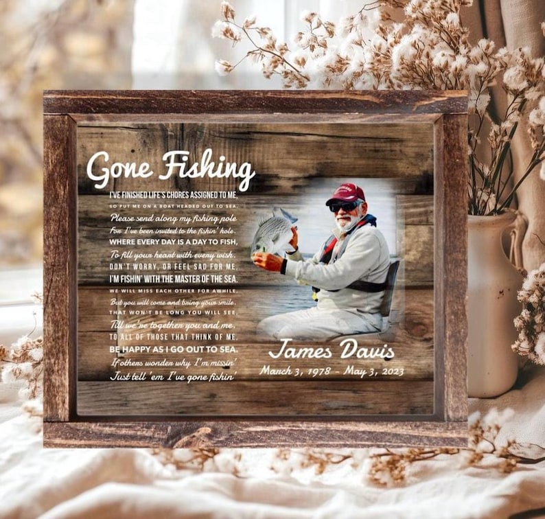K&ouml;nnte beinhalten: Ein rechteckiges Holzschild mit rustikalem Holzmaserungshintergrund, einem Foto einer Person, die einen Fisch h&auml;lt, und dem Text Gone Fishing. Es enth&auml;lt ein Gedicht, den Namen James Davis und die Daten 3. M&auml;rz 1978 - 3. Mai 2023.