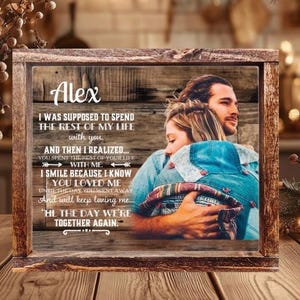 May include: A rectangular wooden frame containing a printed image of a couple embracing. The print features a rustic wood-grain background with the name Alex and a memorial quote about love and loss. The frame has a dark, weathered wood finish.