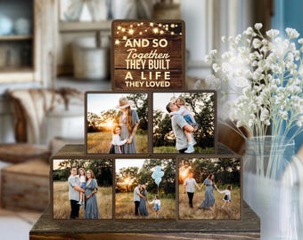 May include: A wooden photo display featuring six family photos. The top section has the text "AND SO TOGETHER THEY BUILT A LIFE THEY LOVED" with small lights. The photos show a family in a field at sunset. The display is on a wooden base.