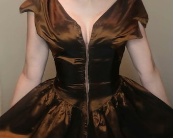 May include: A metallic bronze-colored dress featuring a deep V-neckline, short cap sleeves, and a central vertical zipper closure. The bodice is fitted, transitioning into a full, gathered skirt with a lustrous, reflective finish throughout.