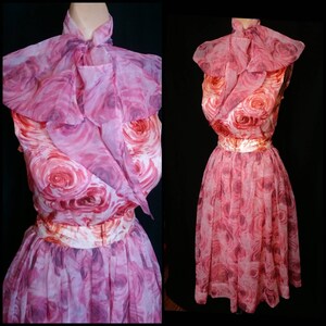 May include: A pink and white floral dress with a ruffled collar and a matching belt. The dress is made of a sheer fabric and has a full skirt.