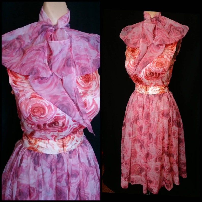 May include: A pink and white floral dress with a ruffled collar and a matching belt. The dress is made of a sheer fabric and has a full skirt.