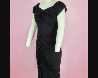 May include: A black, knee-length dress with a ruched bodice and short sleeves. The dress is fitted and has a simple, elegant design.