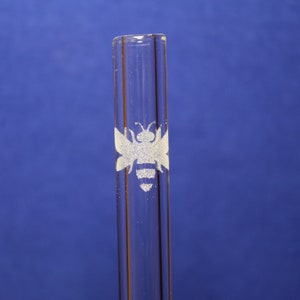 May include: A clear glass drinking straw with a white etched bee design.