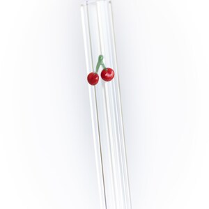 May include: A clear glass drinking straw with a red cherry charm at the top.