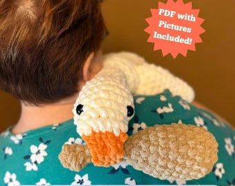 May include: A crocheted white duck with an orange beak and black eyes rests on a person's shoulder. The duck is made of a soft, textured yarn. The image includes the text "PDF with Pictures Included!" and "PATTERN ONLY; NO PHYSICAL ITEMS".