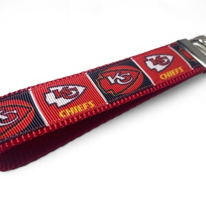 May include: Red, white, and black key chain with the Kansas City Chiefs logo and the word "Chiefs" repeated on the ribbon. The key chain has a silver metal key ring.