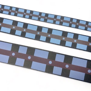 May include: Three different widths of black and blue patterned ribbon with brown accents. The ribbon has a geometric design with squares and circles.
